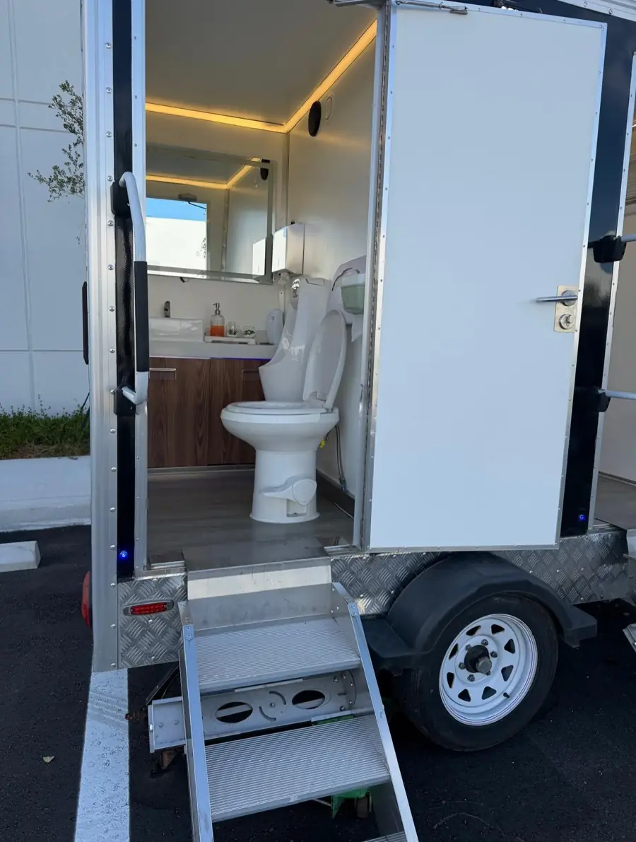 Restroom trailer with door open showing a flush toilet, wood vanity and LED lighting