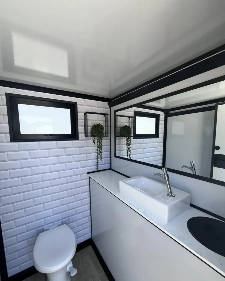 Restroom trailer interior with white tile, sink, mirror and plants