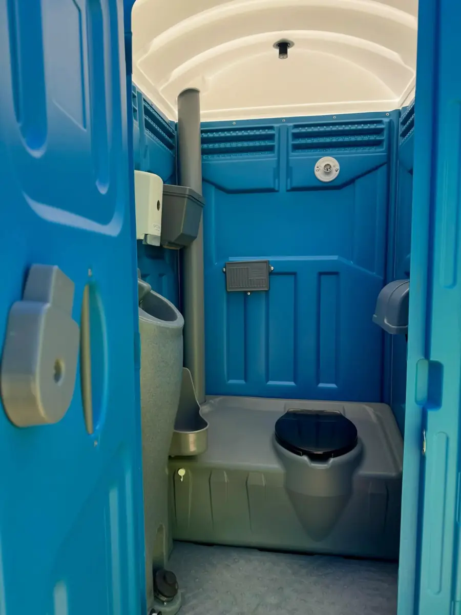 Blue standard porta potty interior showing the urinal and vent pipe beside the seat