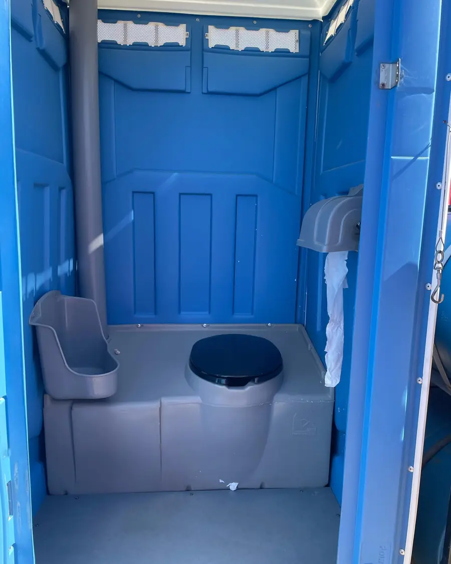 Inside a blue standard porta potty showing the seat, urinal and toilet paper