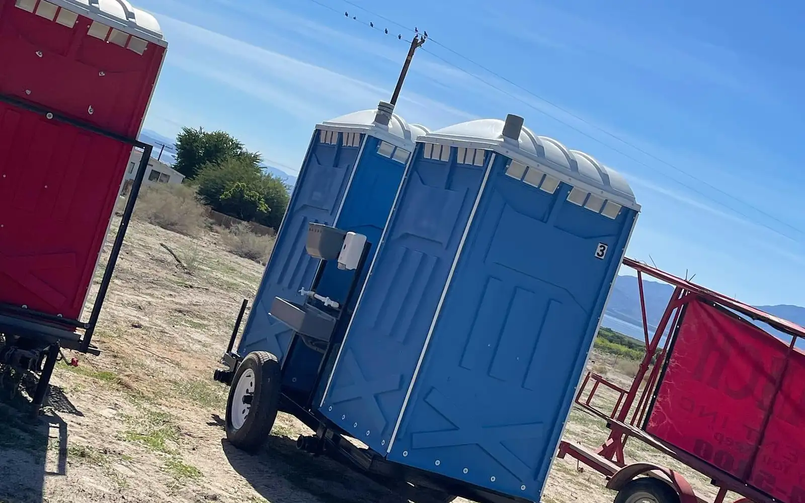 Towable trailers carrying porta potties at a dirt field site