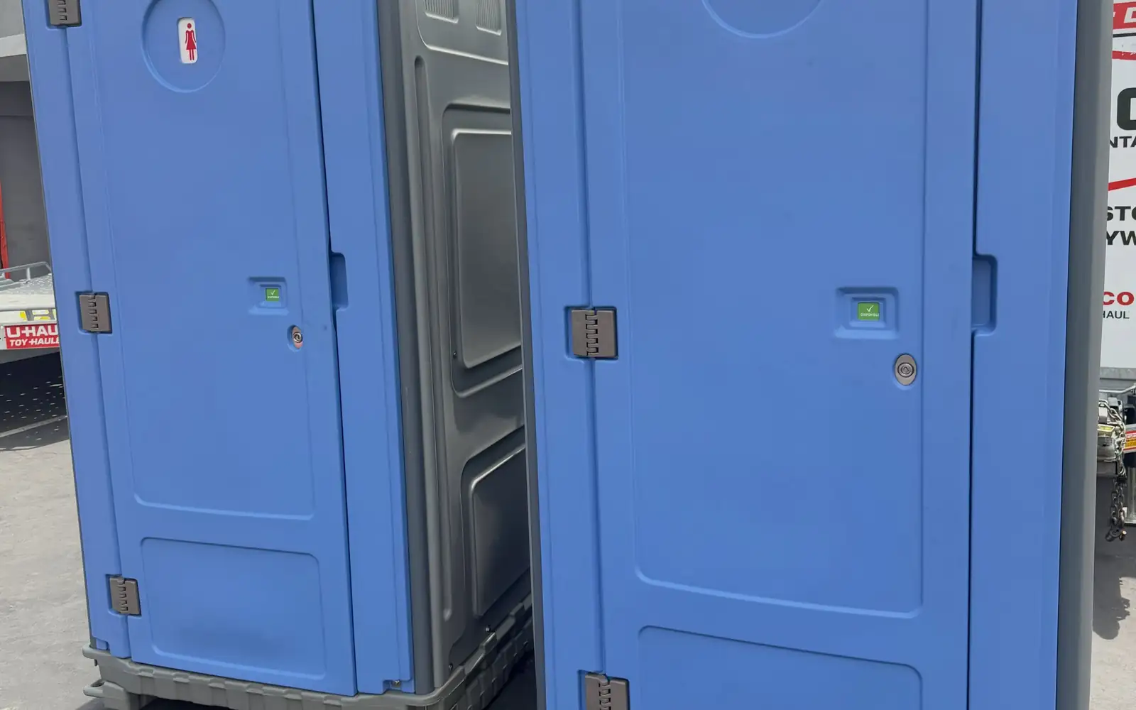 Two blue standard porta potties in a paved loading yard