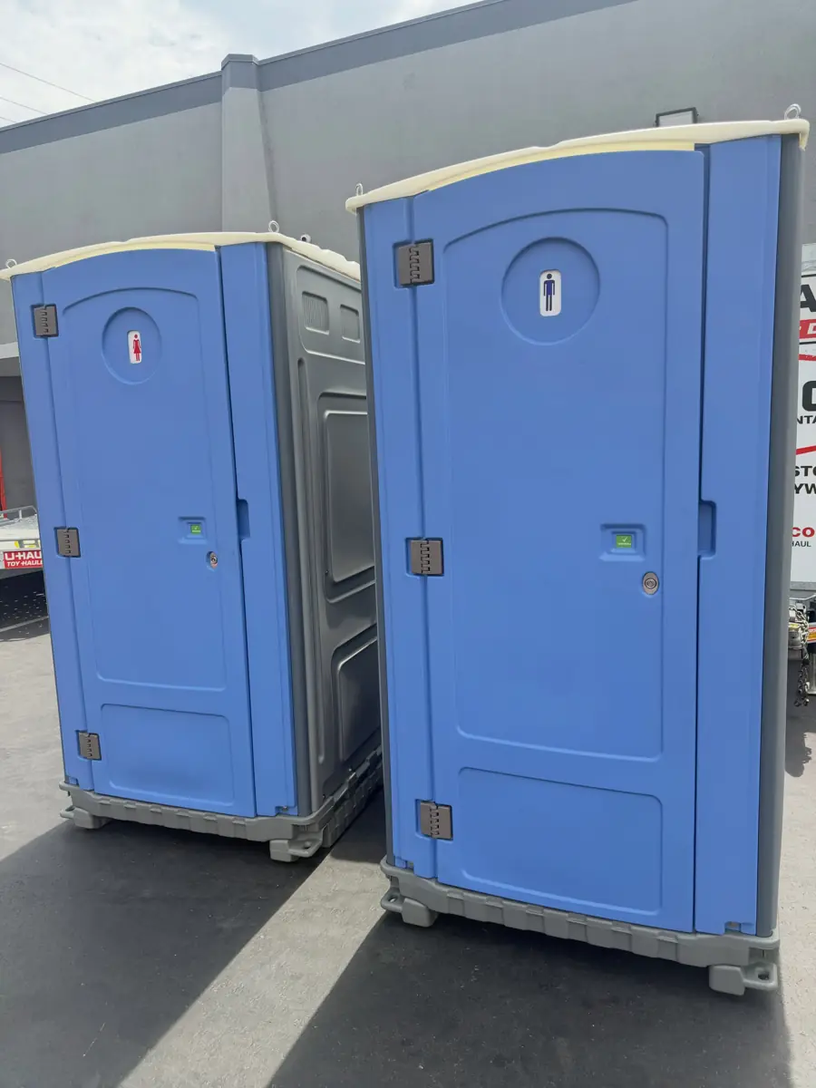 Two blue standard porta potties in a paved loading yard