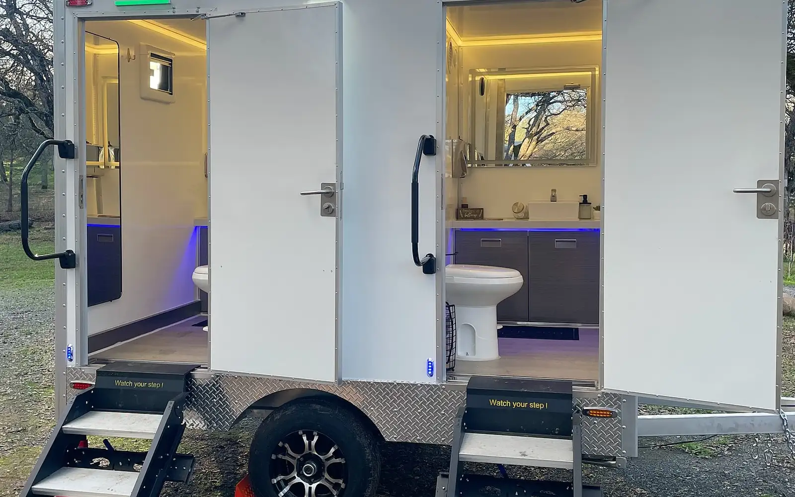 Two-room luxury restroom trailer with open doors and steps on gravel