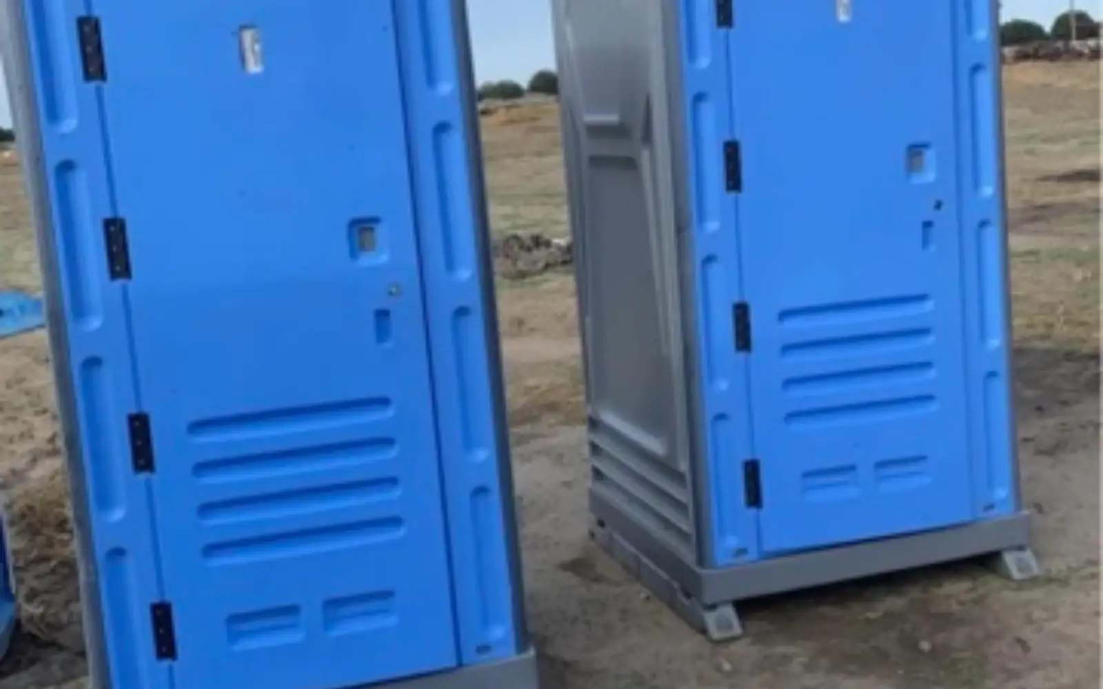 Blue and gray standard porta potties on a dirt construction lot